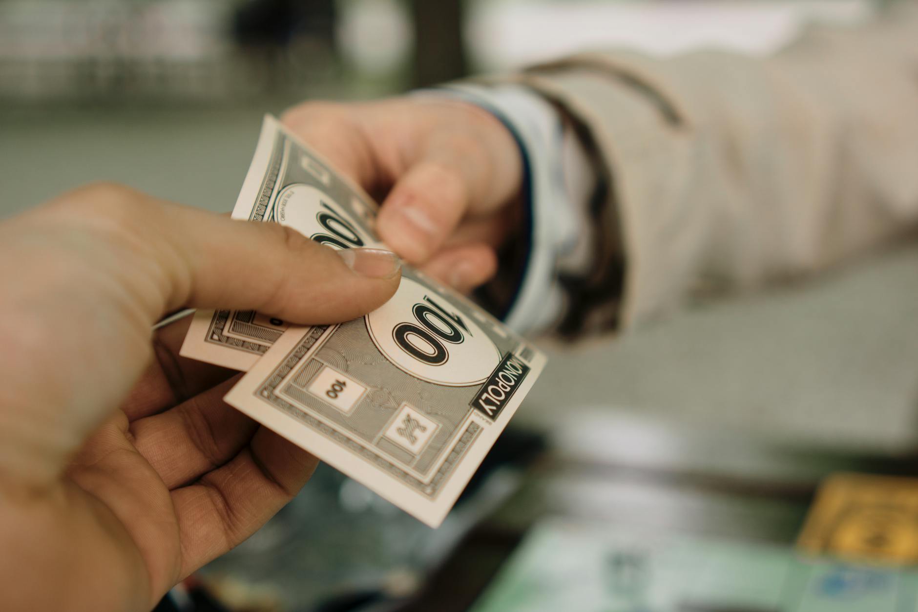 Dłonie przekazujące banknoty Monopoly jako symbol negocjacji ceny