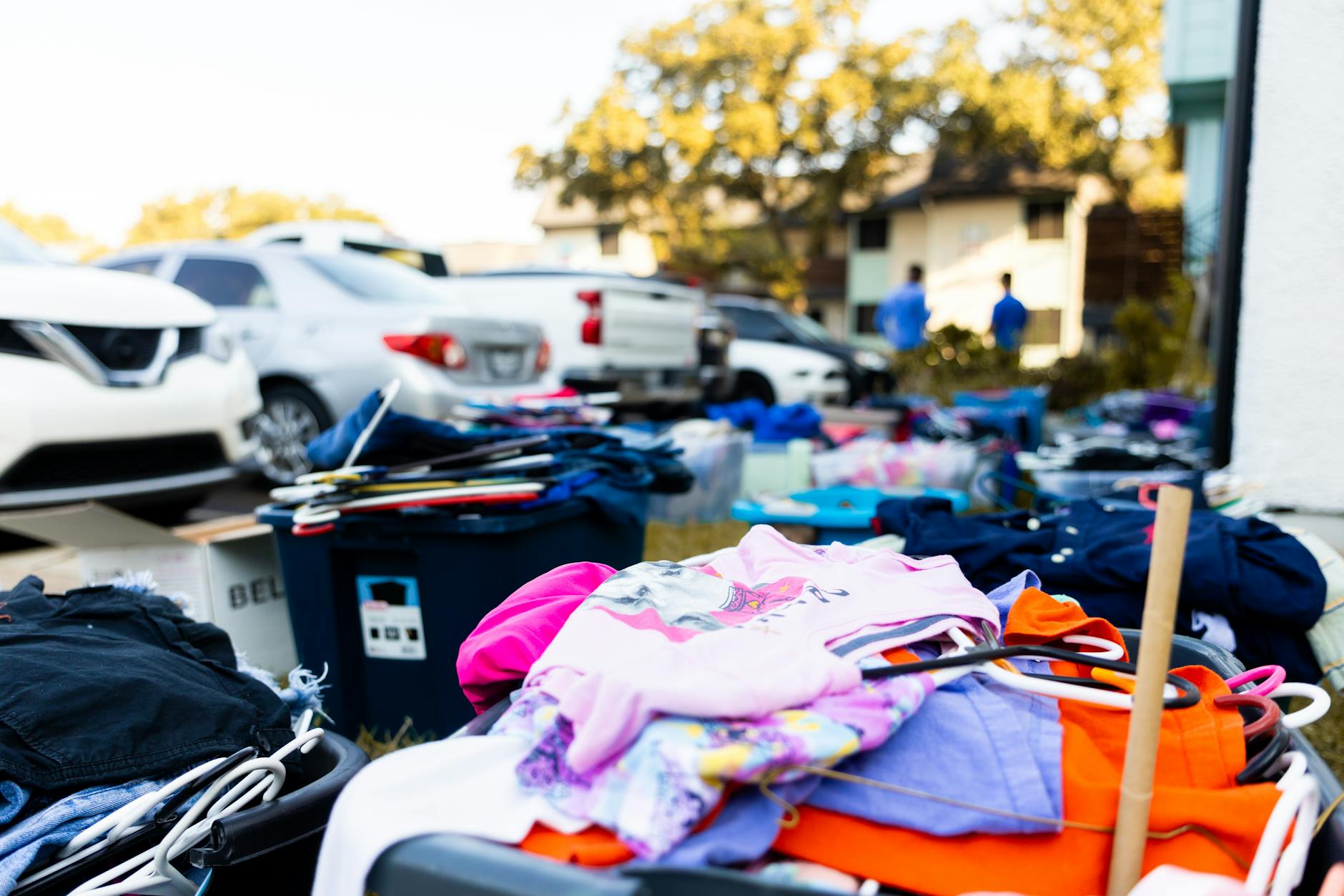Wyprzedaż garażowa na podjeździe z ubraniami i samochodami w tle