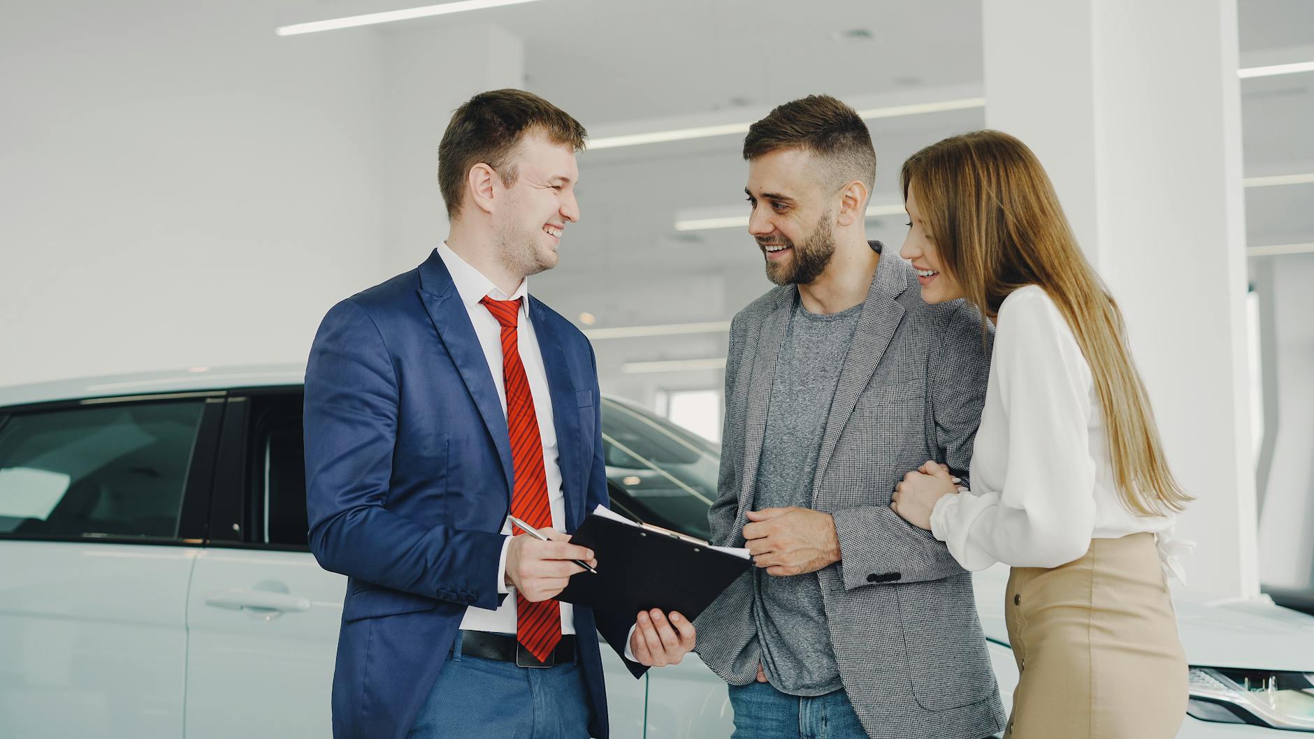 Uśmiechnięta para kupuje samochód od sprzedawcy w salonie